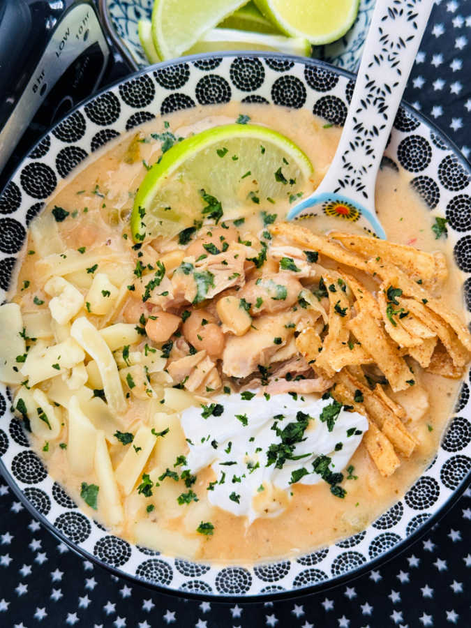 a bowl of creamy white chicken chili garnished with cheese, tortilla chips and sour cream