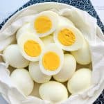 a bowl of a dozen eggs just peeled, with two of them sliced in half