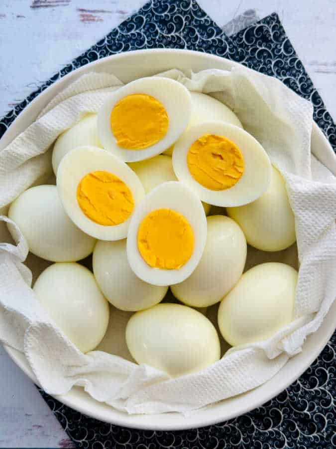 a bowl of one dozen hard boiled eggs with two of then sliced in half