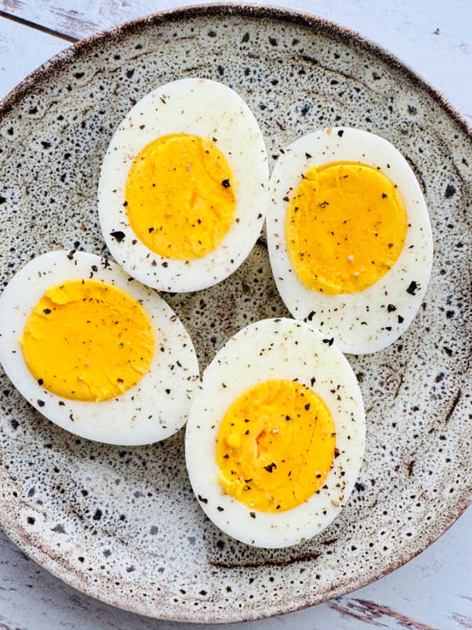 two hard boiled eggs sliced in half on a plate and topped with salt and cracked pepper