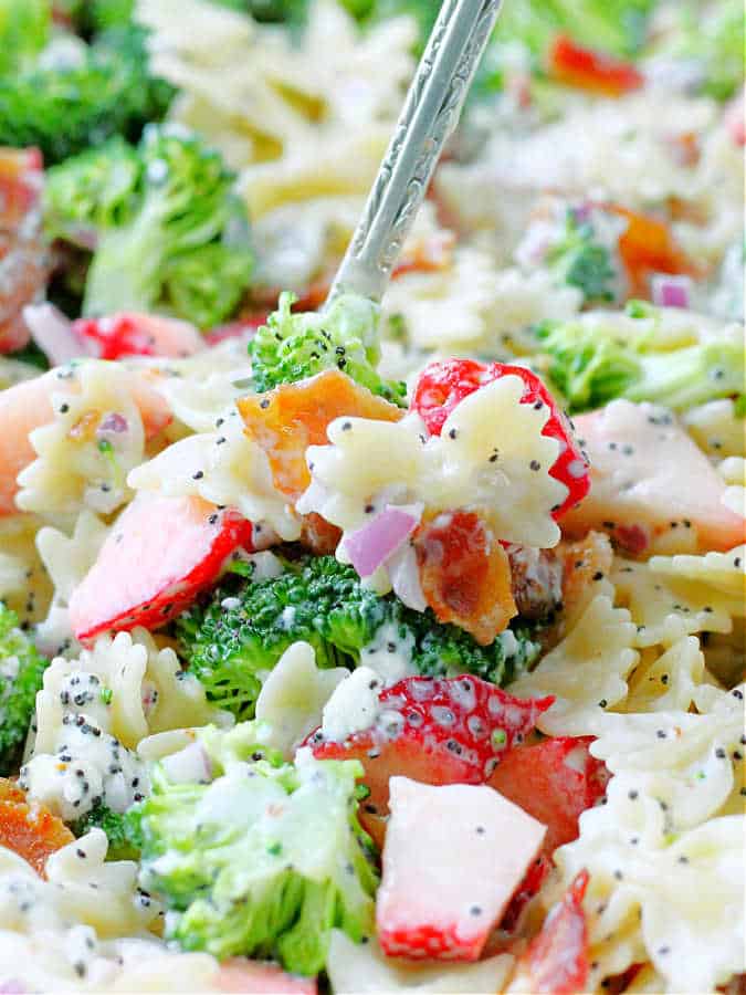 a spoonful of summer broccoli pasta salad with bowtie pasta, broccoli, strawberries and bacon