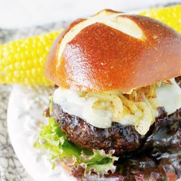 Grilled bourbon burger on a plate with a pretzel bun and an ear of corn on the cob