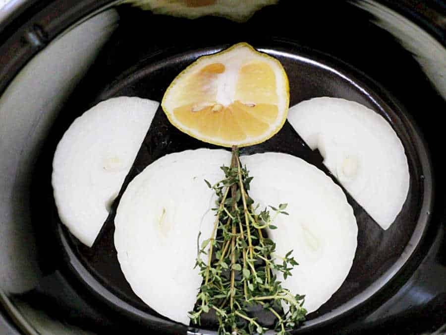 onion lemon and thyme in the bottom of a slow cooker insert