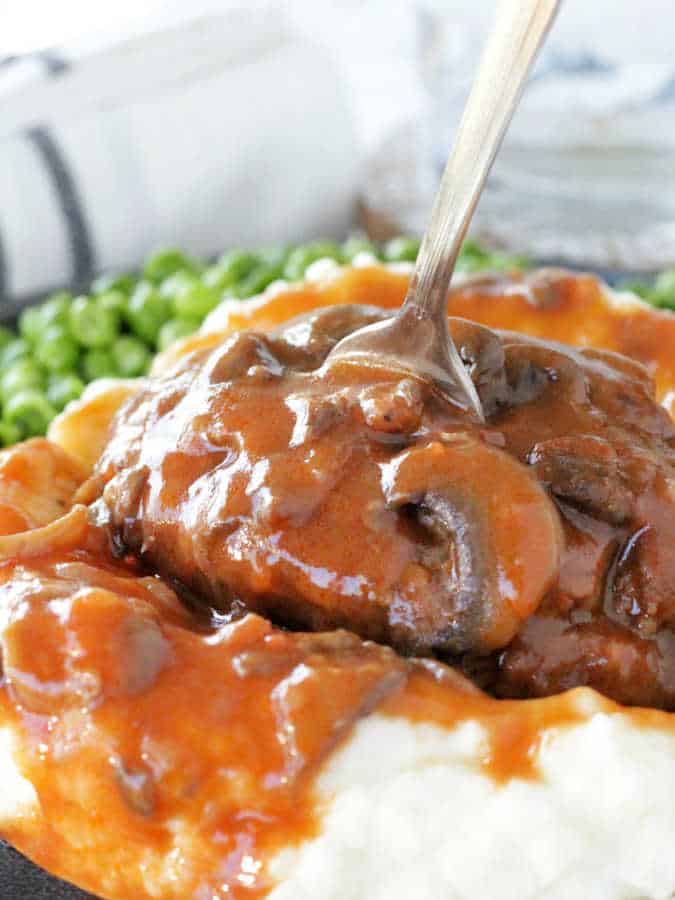 salisbury steak served atop a pile of mashed potatoes and smothered in a rich mushroom gravy