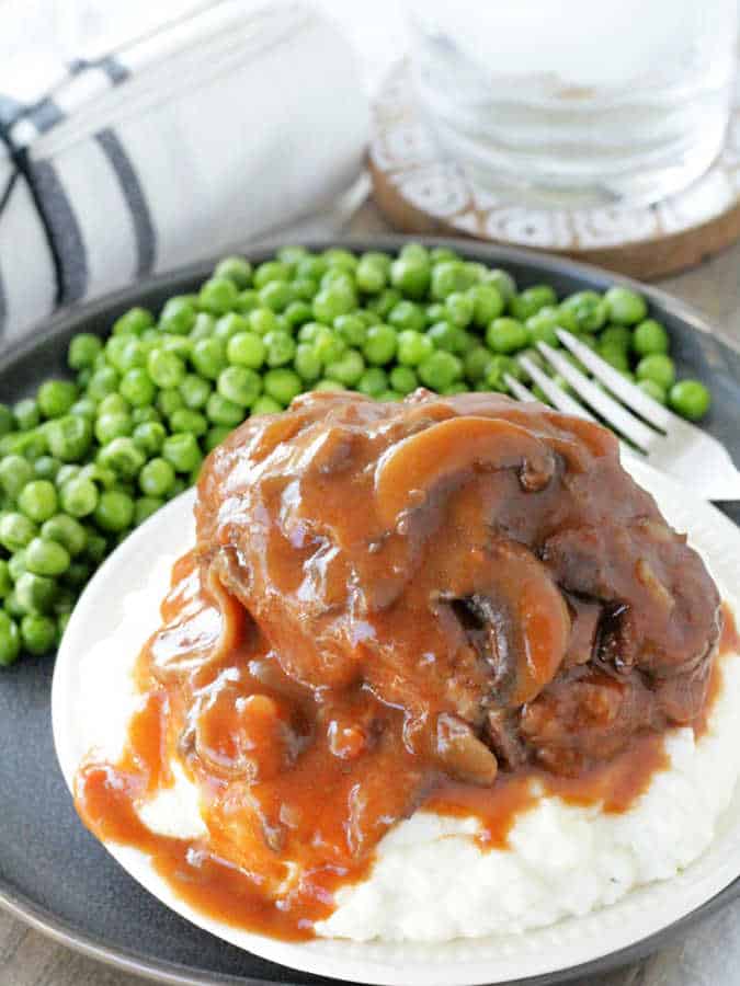 salisbury steak and mashed potatoes plated and smothered with mushroom gravy with a side of peas