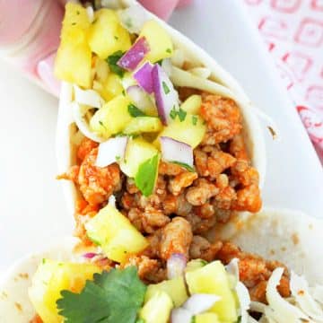 holding a prepared ground pork taco with pineapple salsa, ready to take a bite