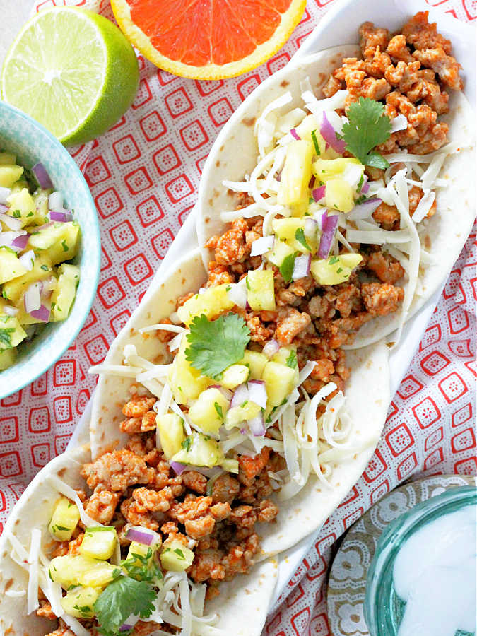 three ground pork tacos on a platter topped with fresh pineapple salsa and Pepper Jack cheese