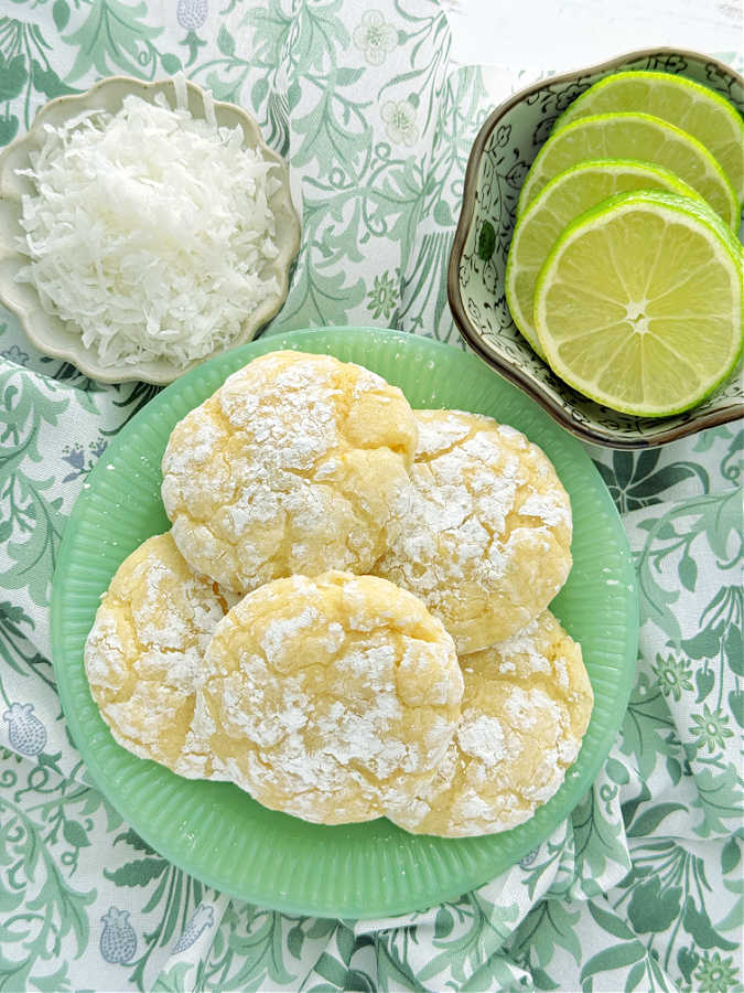 key lime crinkle cookies on a green glass plate with a bowl of coconut and slices of lime