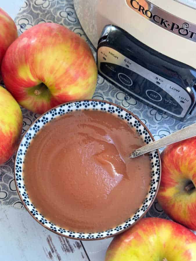 a bowl full of crockpot applesauce sitting in front of the Crock-Pot it was cooked in a surrounded by fresh apples