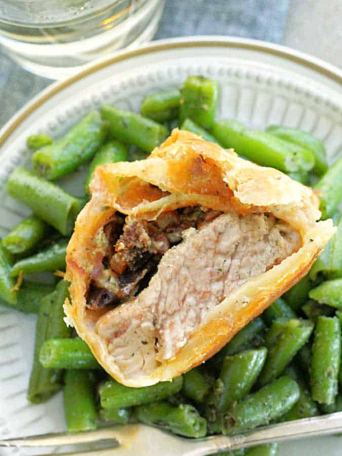 a pork wellington cut in half plated with green beans