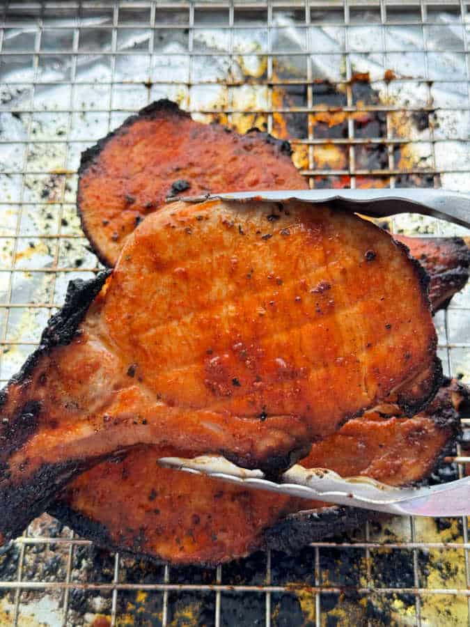 holding a freshly broiled pork chop with metal serving tongs