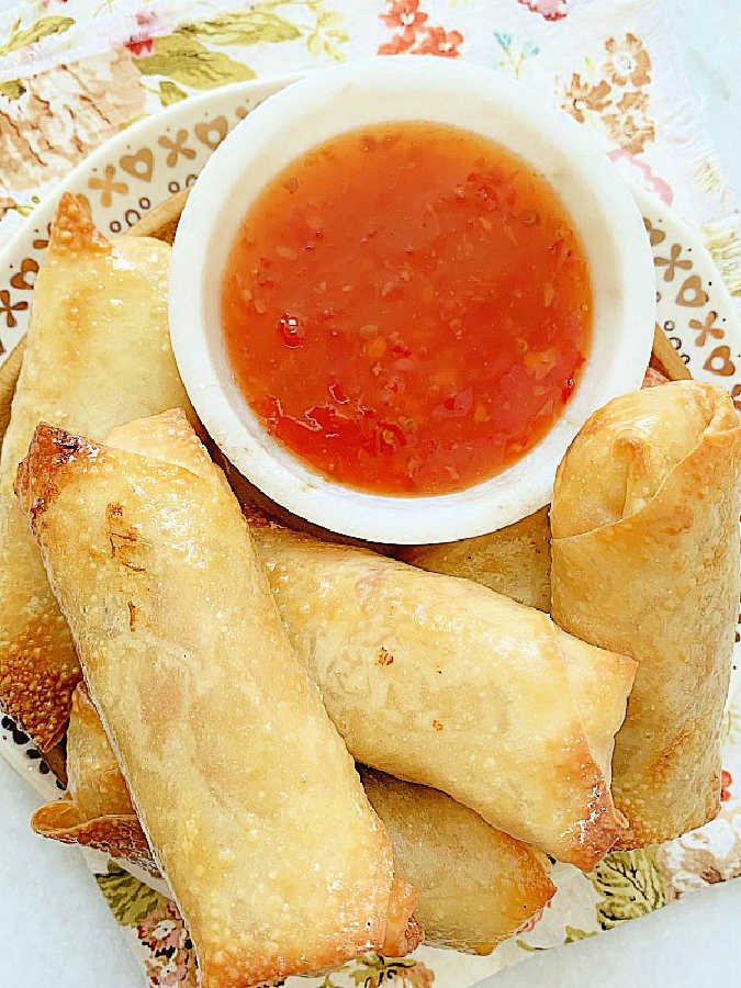 a plate of six air fried egg rolls with a small bowl of sweet chili sauce to dip