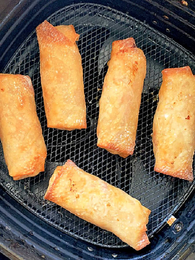 five freshly cooked egg rolls in the basket of air fryer