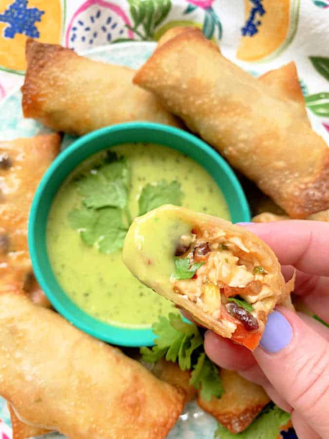 dipping an egg roll into a small green bowl of avocado salsa