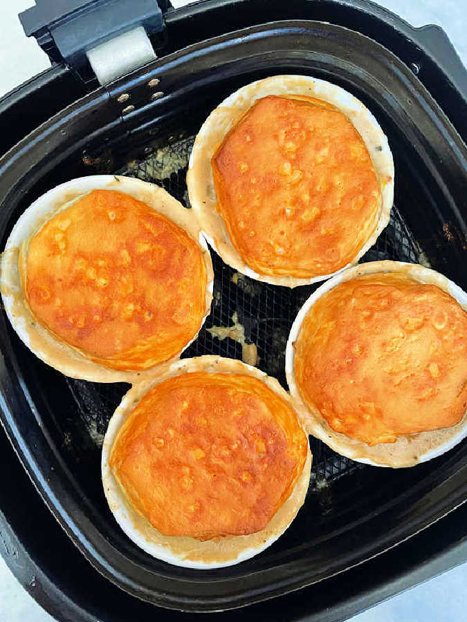 four freshly cooked pot pies topped with biscuits in the basket of an air fryer