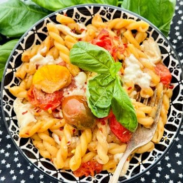 a black and white serving bowl filled with creamy tomato burrata pasta and garnished with fresh basil