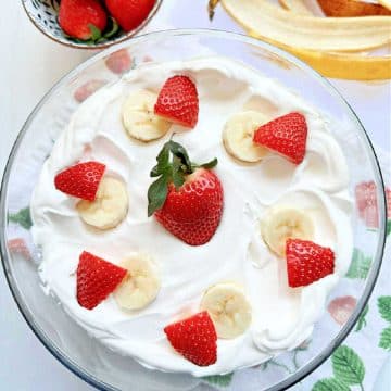 strawberry banana pudding in a clear glass trifle bowl, garnished with fresh berries and sliced bananas