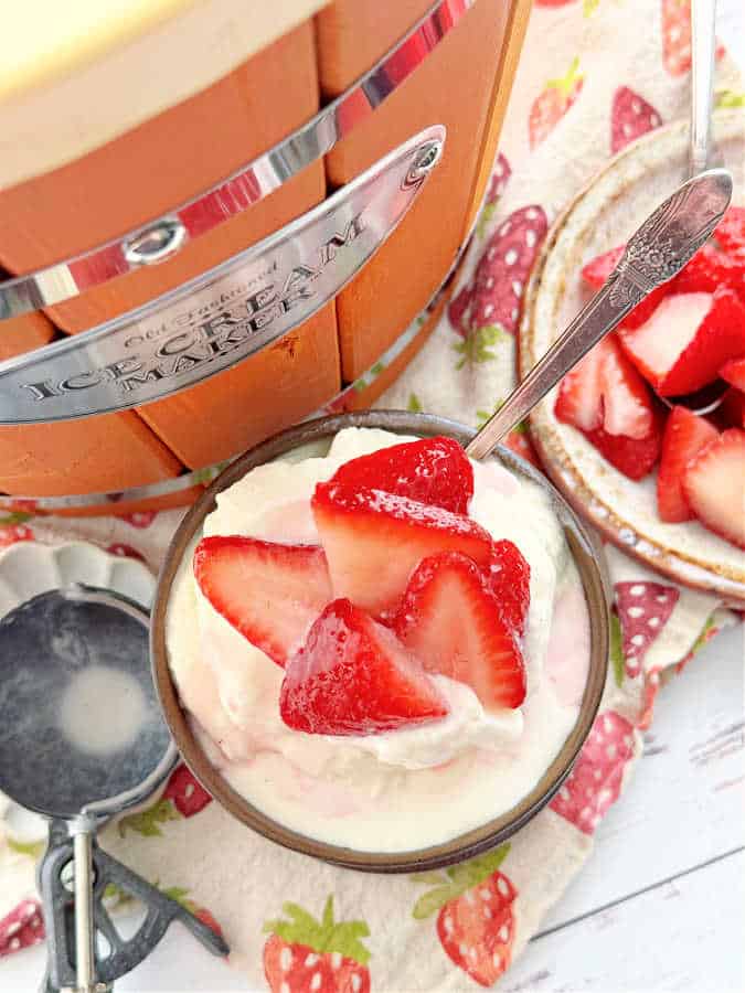overhead shot of the nostalgia wooden bucket style ice cream maker pictured with a bowl of homemade vanilla ice cream topped with fresh sliced strawberries