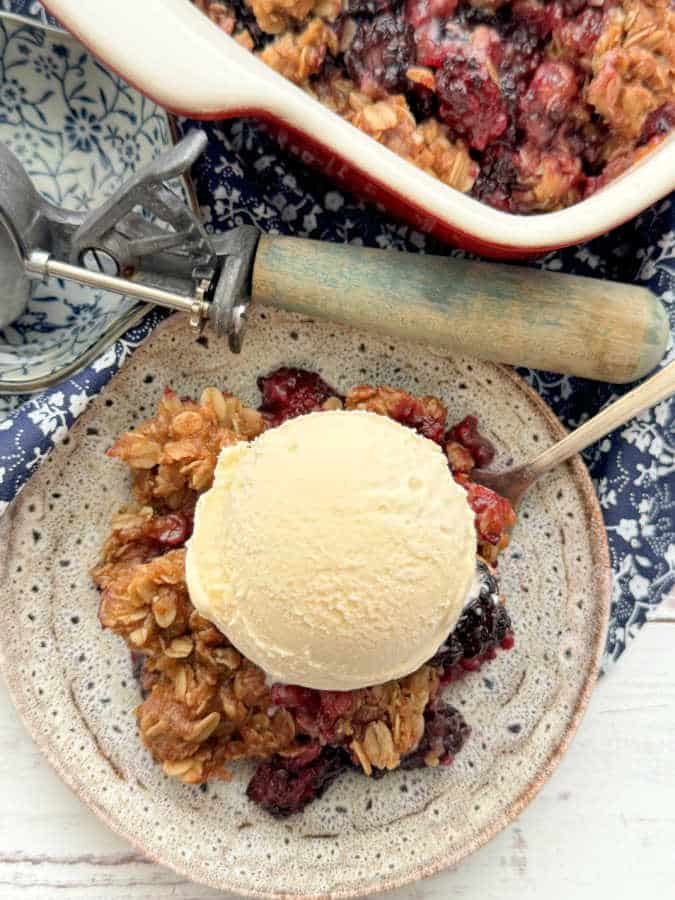 a dish of blackberry crisp topped with a scoop of vanilla ice cream