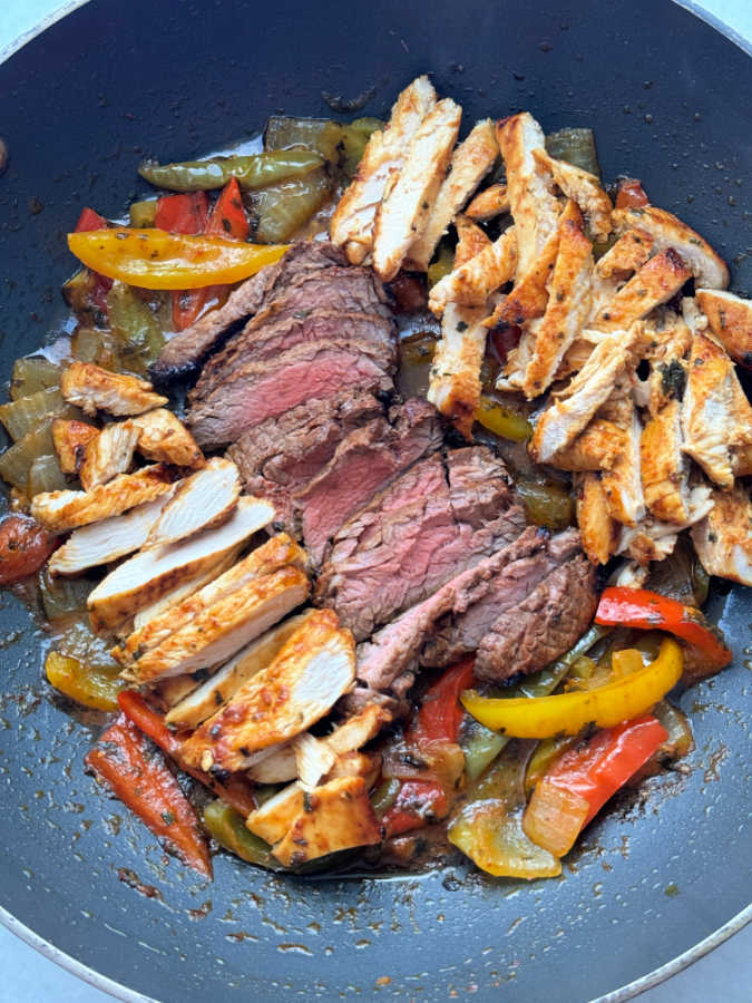 air fryer fajitas with cooked peppers and onions, sliced steak and chicken, ready to serve from the pan