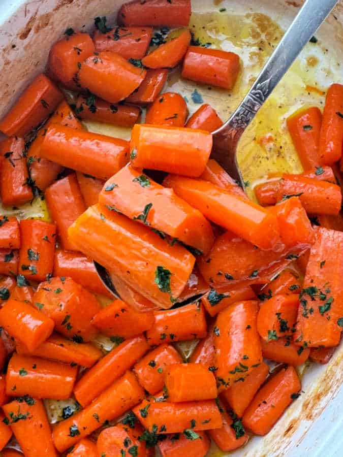 serving a spoonful of glazed carrots from their baking dish