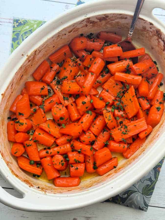 glazed carrots garnished with parsley in a white baking dish ready to serve