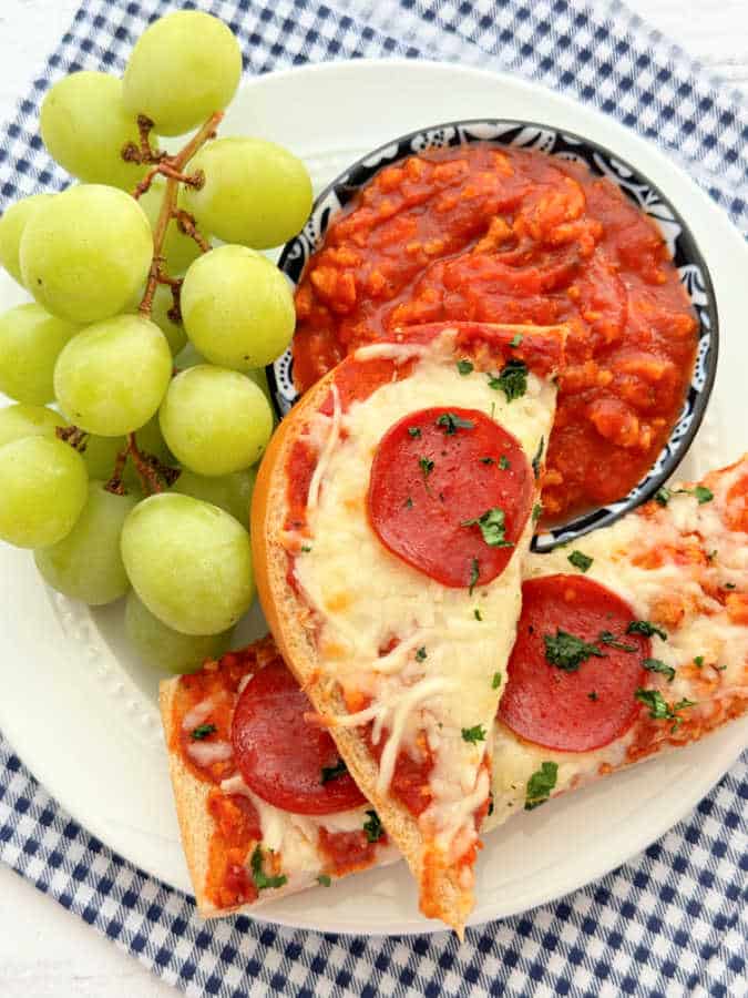 two slices of pizza boat plated with dipping sauce and green grapes