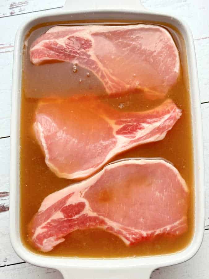 three pork chops soaking in apple cider brine