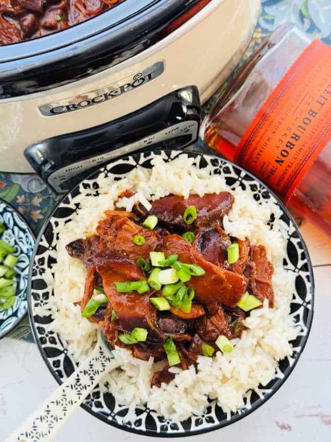 a bowl of rice topped with a serving of bourbon chicken and garnished with green onions