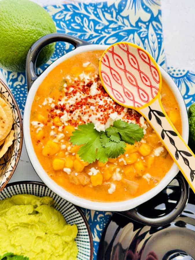 a crock of corn chowder with a side of chips and guacamole