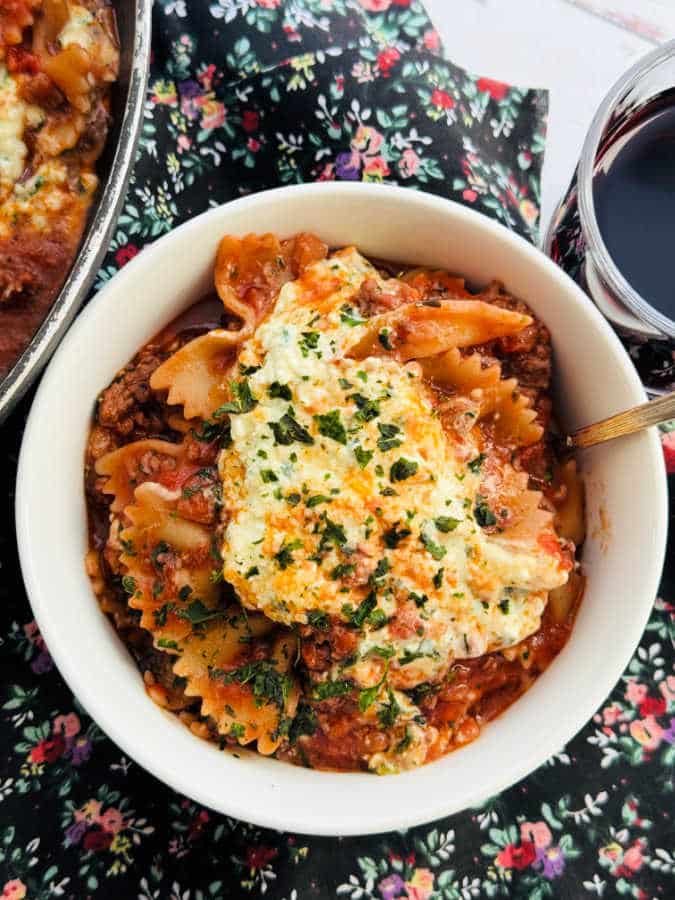 a serving of one pot lasagna in a bowl, with a glass of red wine on the side