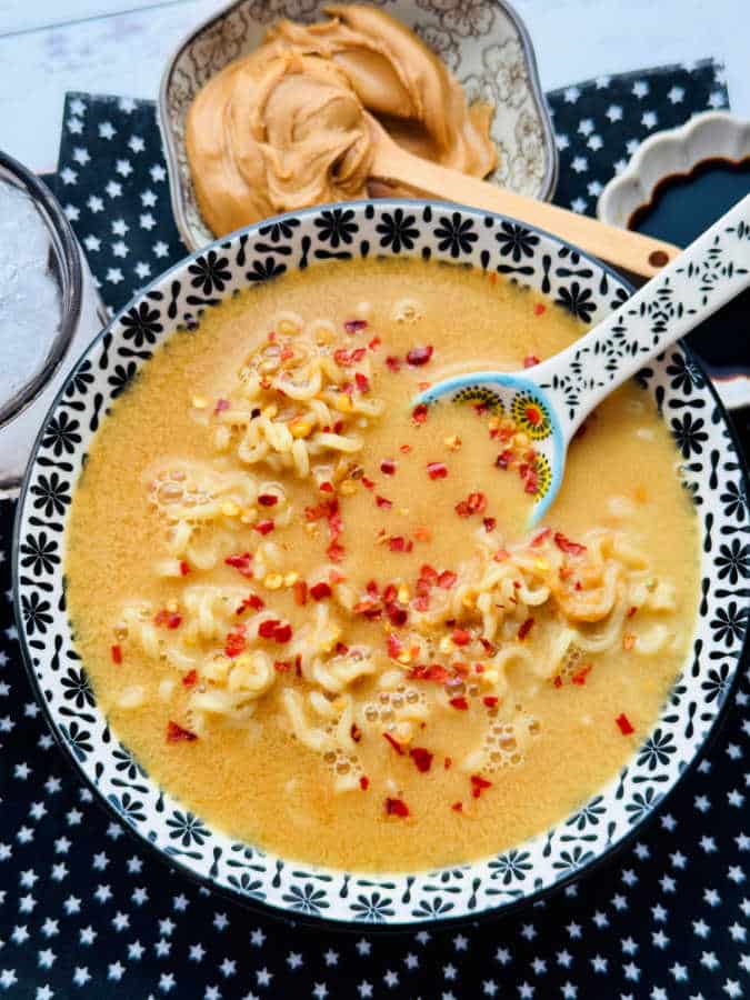 a bowl full of peanut butter ramen noodles ready to eat and garnished with red pepper flakes