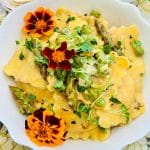 a bowl of ravioli primavera garnished with broccoli sprouts and edible flowers