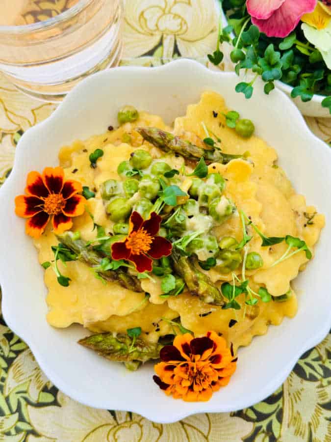 a bowlful of ravioli primavera garnished with broccoli sprouts and edible flowers