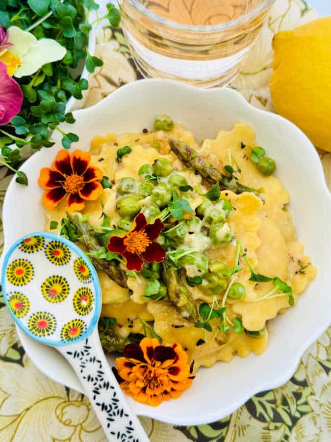 a bowl of ravioli primavera with a decorate spoon and a glass of wine