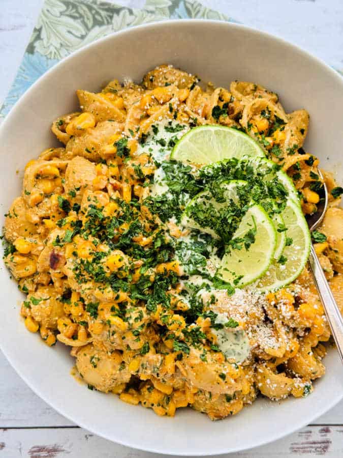 a large white serving bowl with elote pasta salad, garnished with lime slices and fresh cilantro